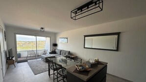 A modern kitchen with a glass dining table, a sofa, and a balcony with a view.
