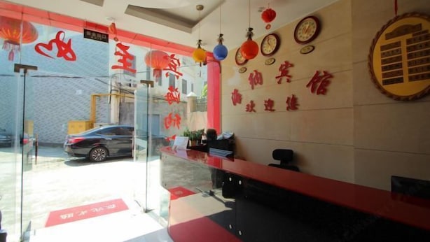 Zona de recepción con puerta de vidrio, mostrador de recepción y pared con caracteres chinos.