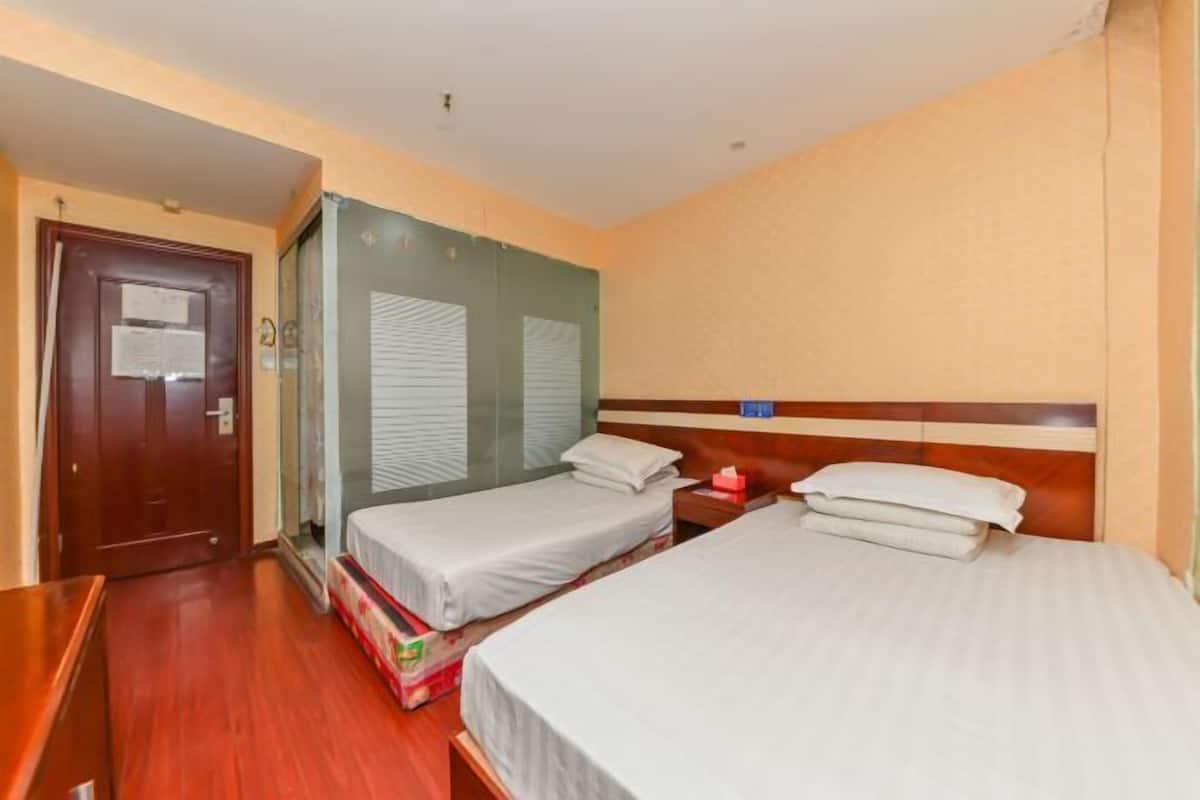 A hotel room with two single beds, a wooden dresser, a door with a notice, and a window with blinds.