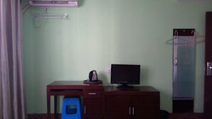 Una habitación con un escritorio de madera, televisor, un taburete azul y un armario.