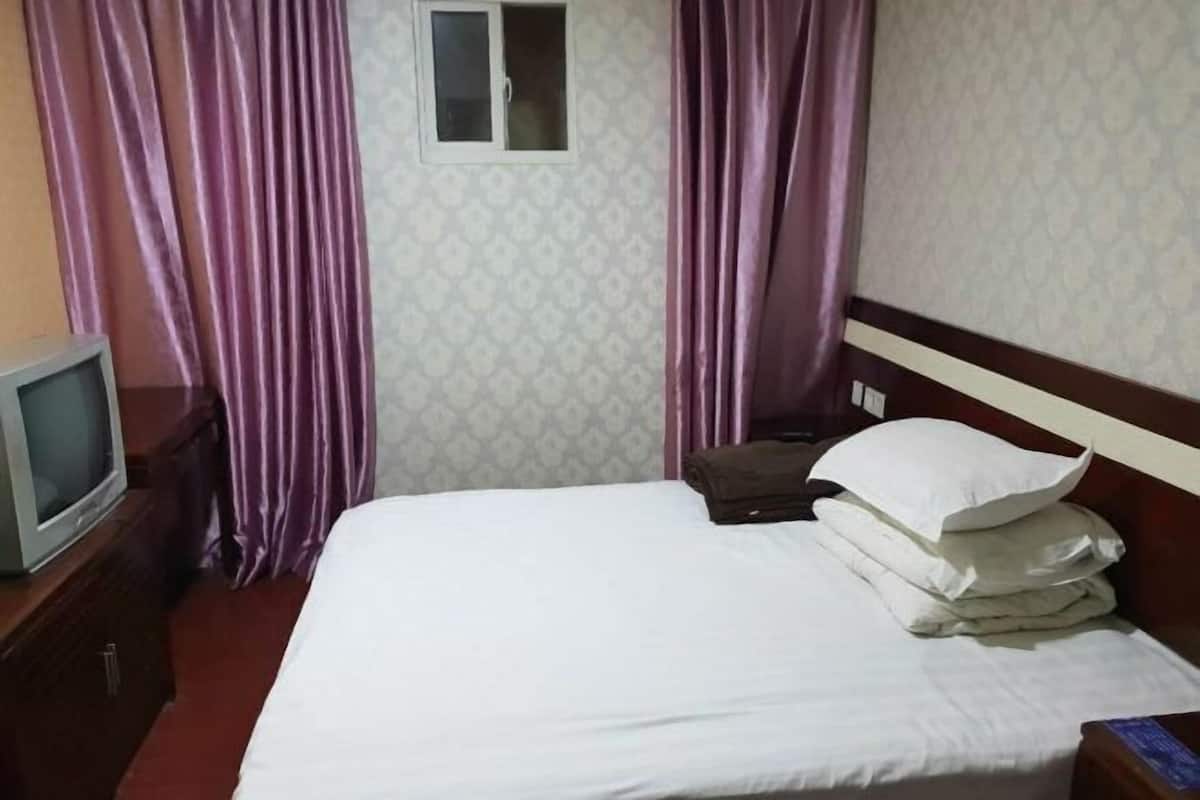 A hotel room with a bed, a television on a nightstand, and purple curtains.