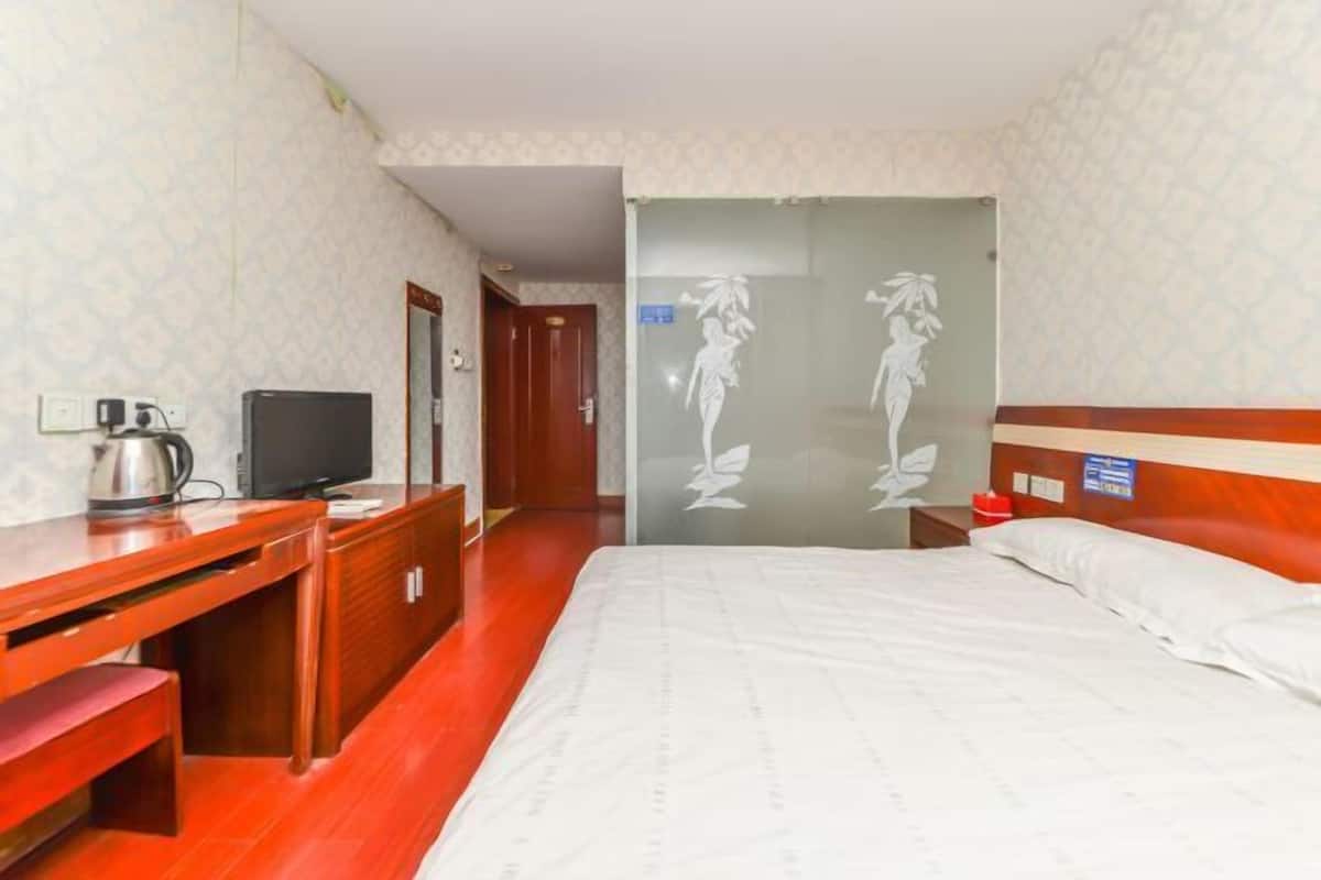 A hotel room with a bed, wooden desk, television, and a mirror.