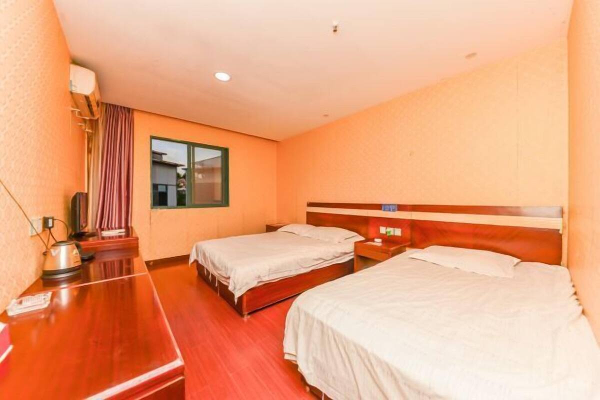 A hotel room with two single beds, a wooden desk, a kettle, and a window with curtains.