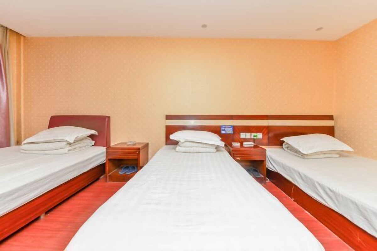 A hotel room with three single beds, a wooden headboard, a nightstand, and a small table with a lamp.