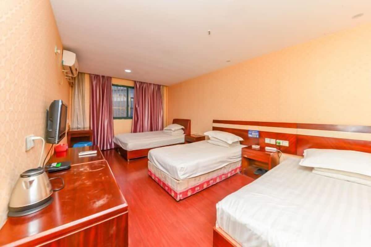 A hotel room with two single beds, a wooden desk with a kettle, a TV, and a window with curtains.