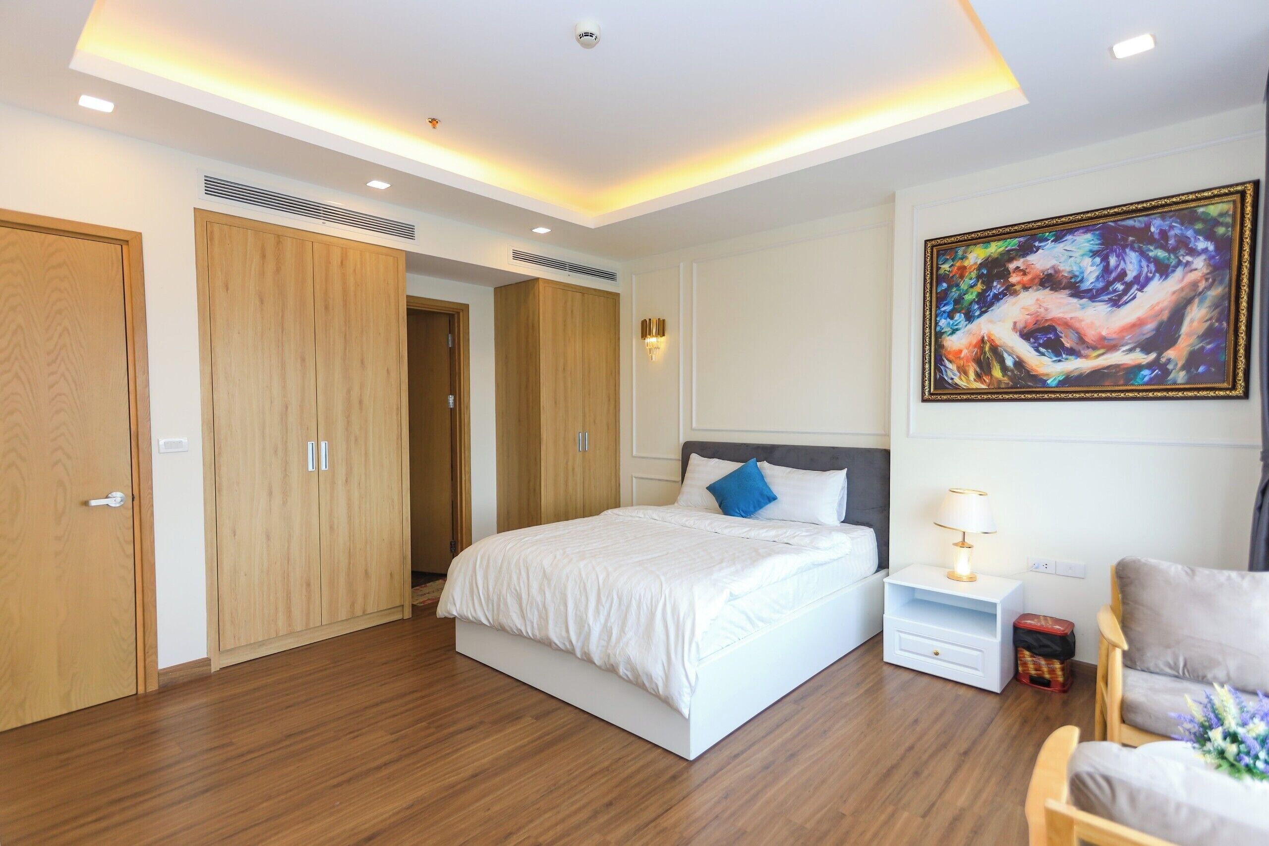 A modern bedroom with a large bed, wooden wardrobe, and a painting on the wall.