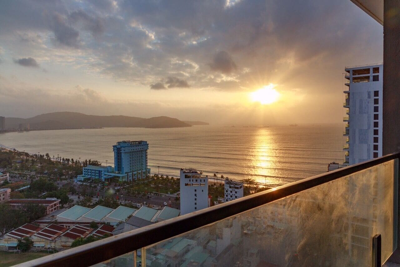 Un paisaje urbano costero con un edificio destacado y vista al mar al atardecer.