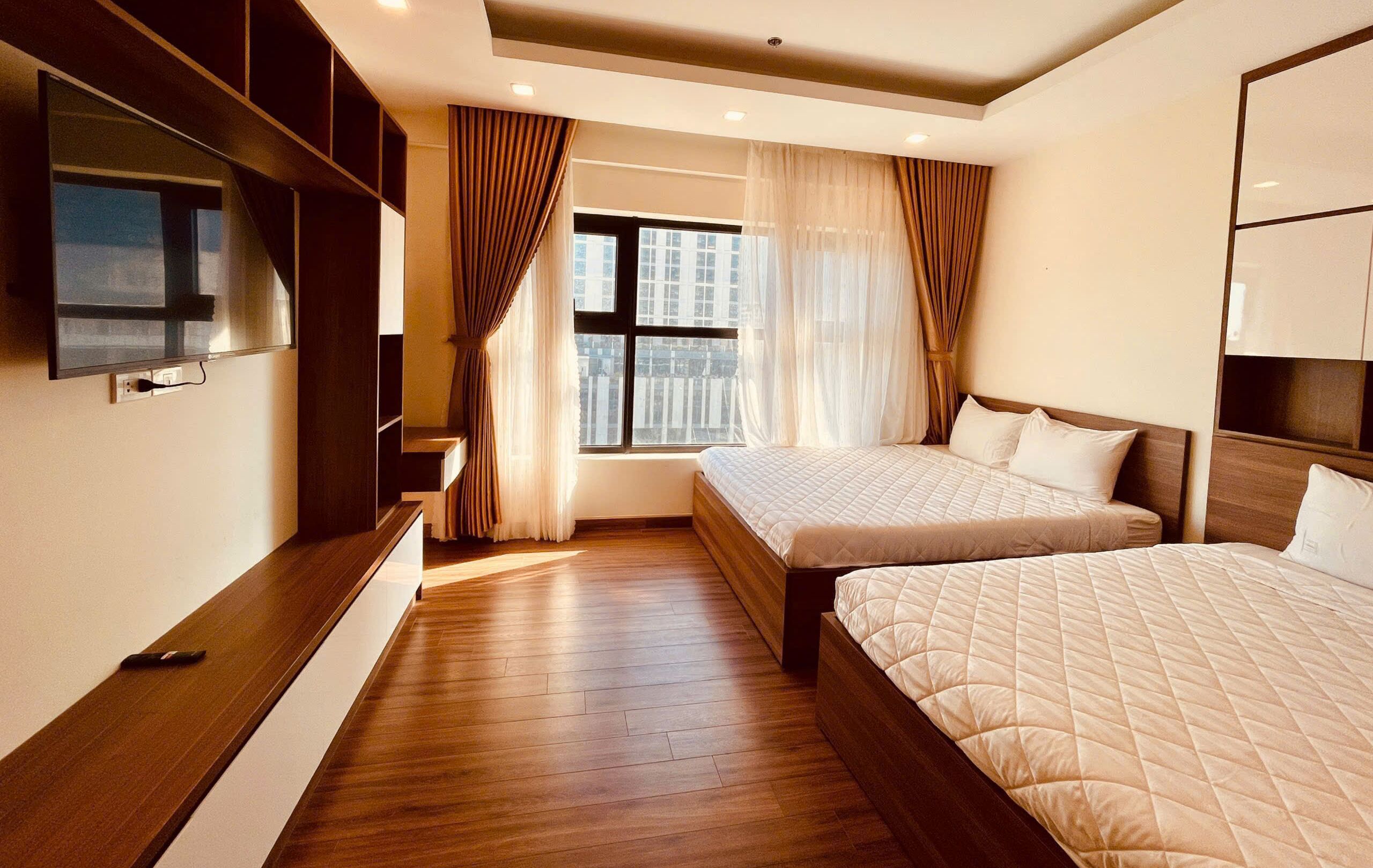 A modern bedroom with two beds, a TV, and a large window with curtains.