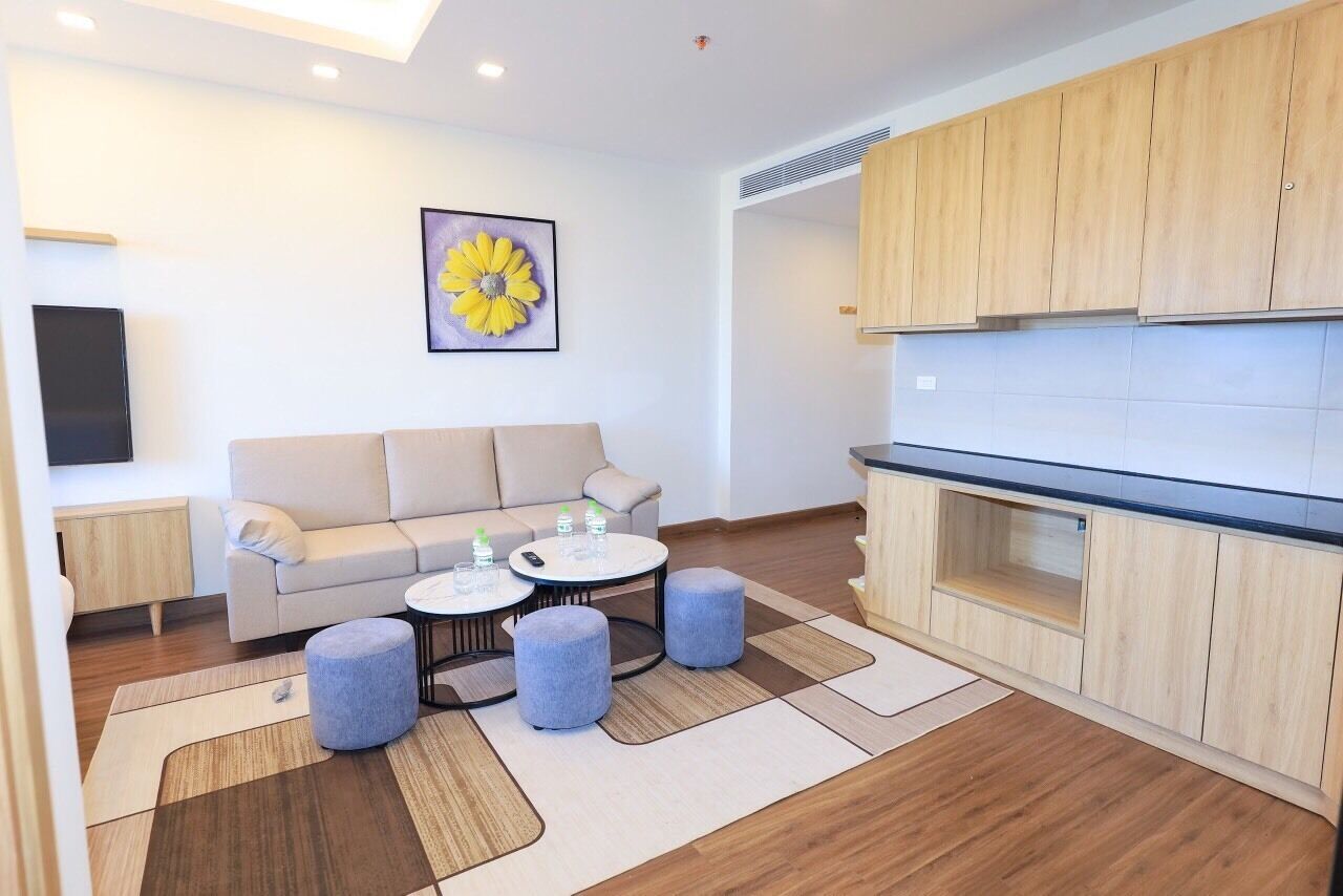 A modern living room with a sofa, ottomans, a coffee table, and a kitchen area with wooden cabinets and a countertop.
