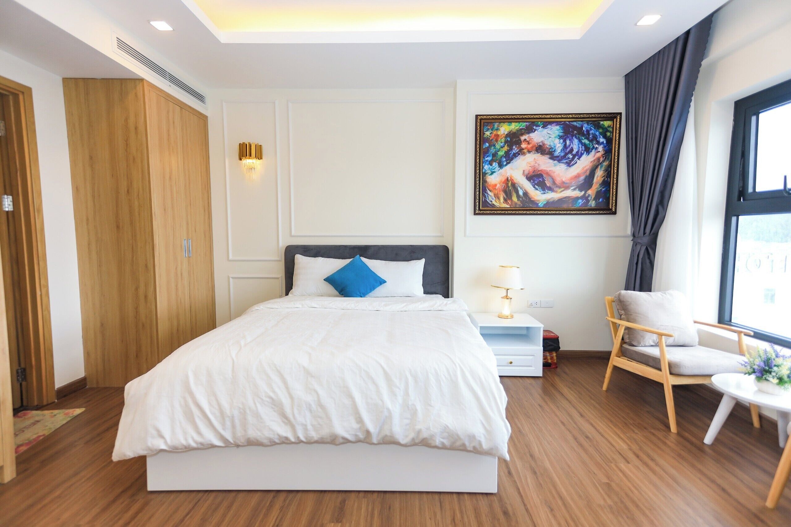 Ein modernes Hotelzimmer mit einem großen Bett, einem Holzschrank, einem Bild an der Wand und einem Fenster mit Vorhängen.