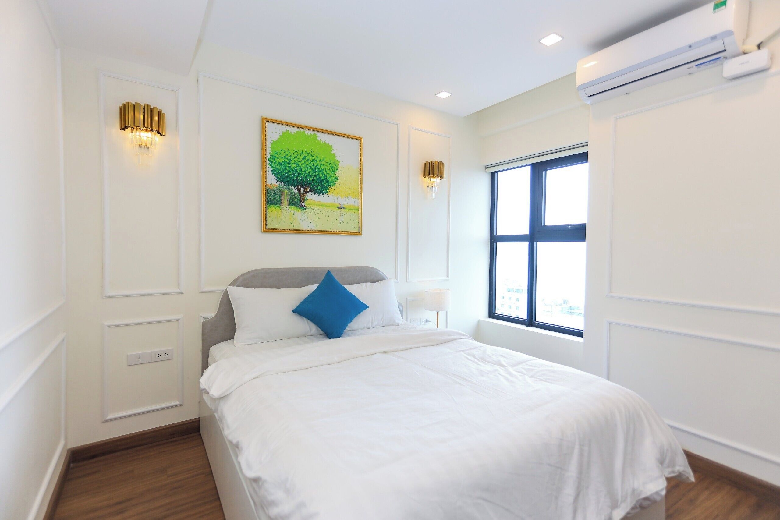 A bedroom with a bed, a window, and a painting of a tree.