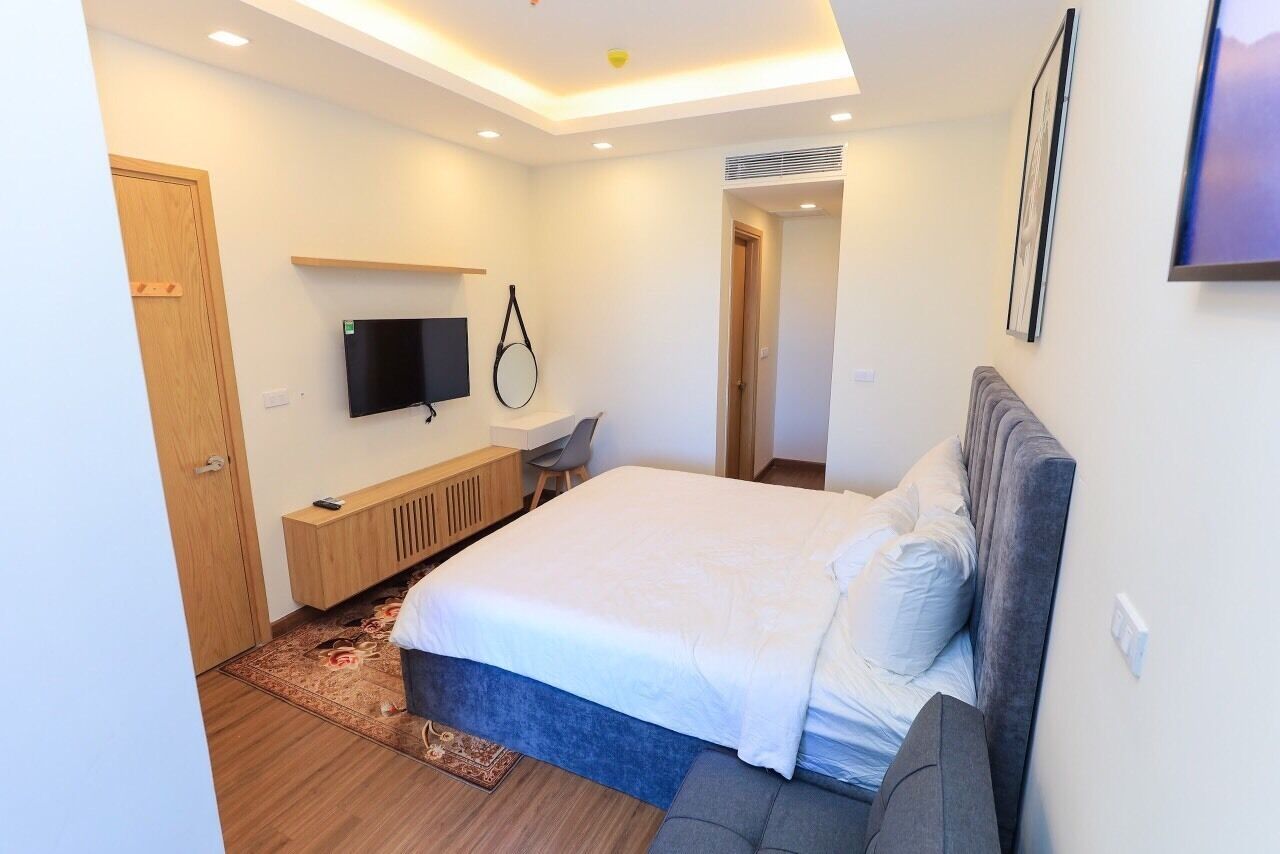 A modern bedroom with a large bed, a TV mounted on the wall, a desk, and a door.
