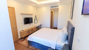 A modern bedroom with a large bed, a TV mounted on the wall, a desk, and a door.