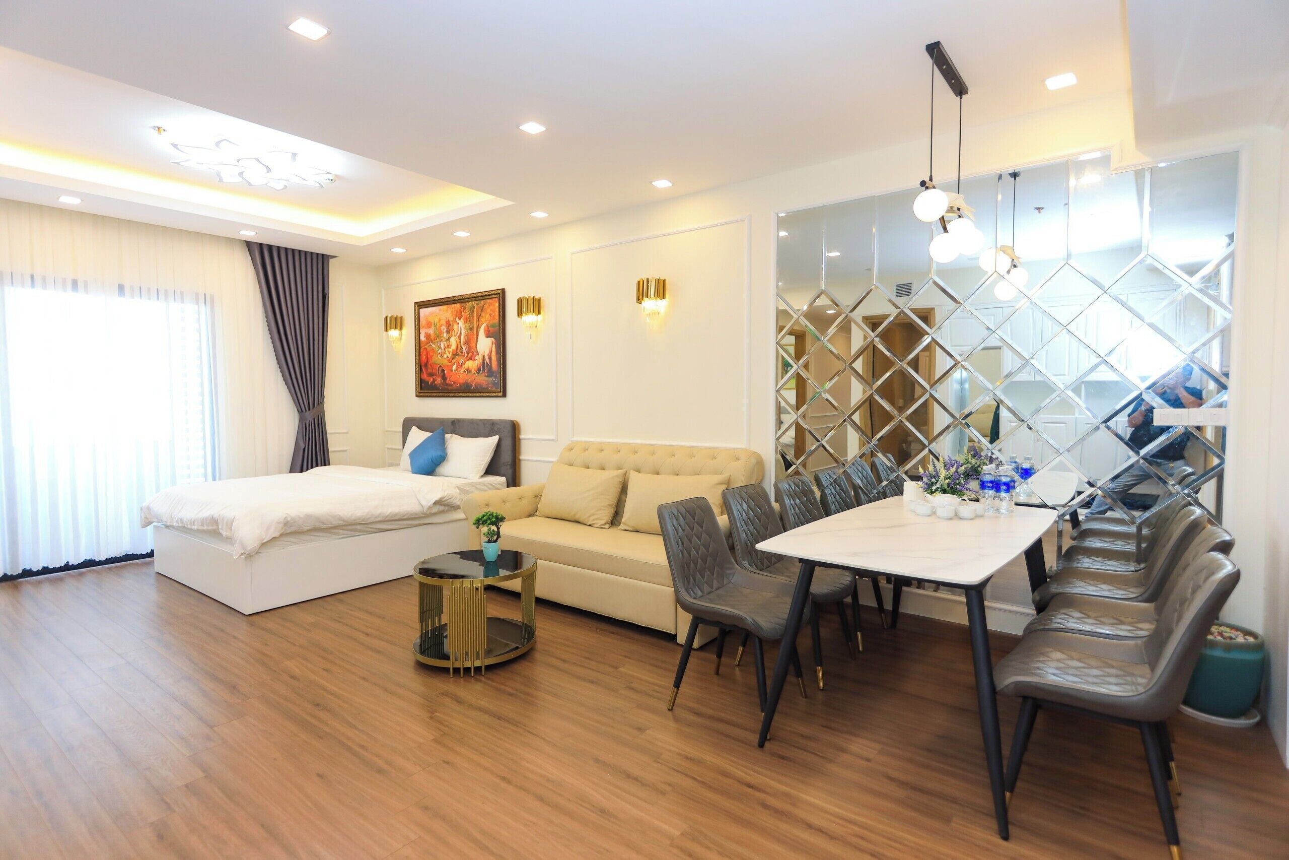 A modern hotel room with a bed, sofa, dining table, chairs, and a decorative wall.