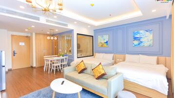 A modern hotel room with a large bed, a sofa, a dining table with chairs, and a chandelier.