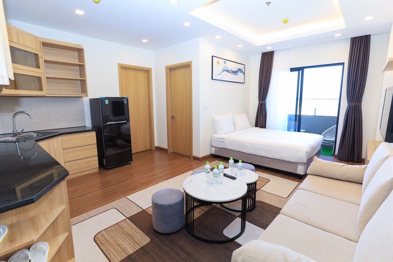 A modern hotel room with a kitchenette, a bed, a sofa, and a view of the outdoors.