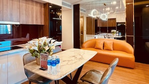 Een moderne hotelkamer met een marmeren eettafel, een bank en een keukenruimte zichtbaar door een glazen wand.
