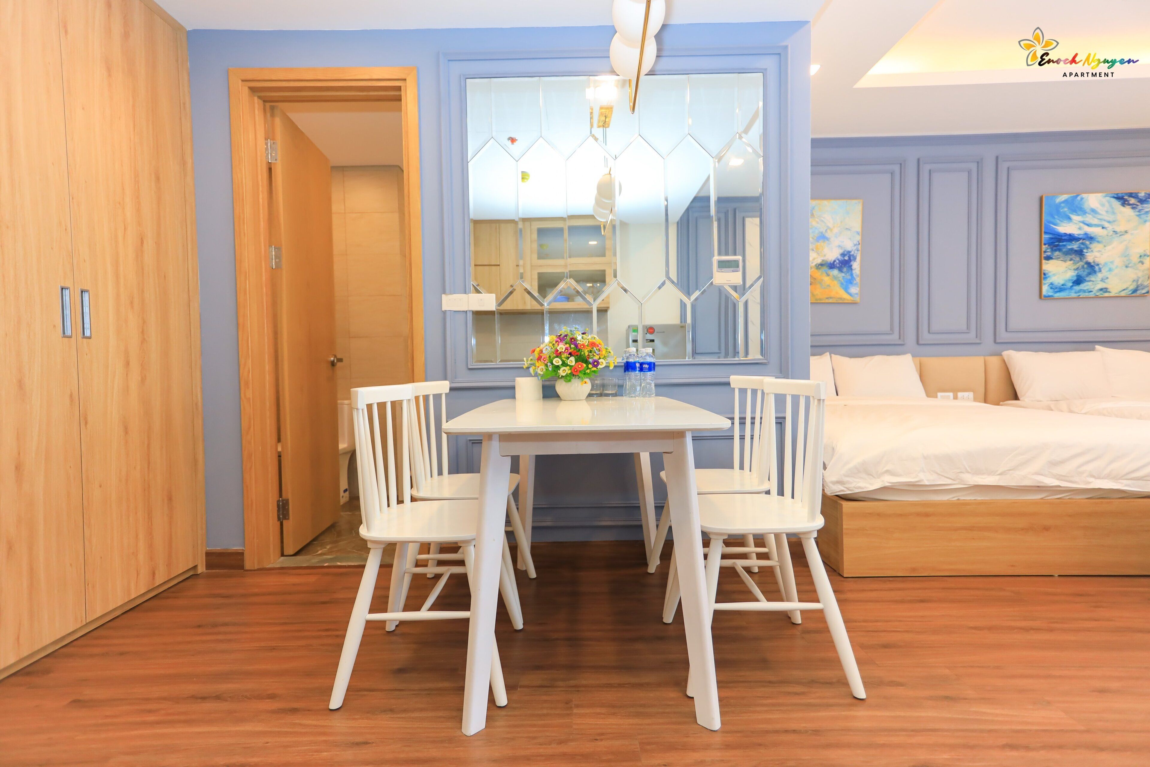 A bedroom with a bed, a wooden wardrobe, a dining table with chairs, and a large mirror.