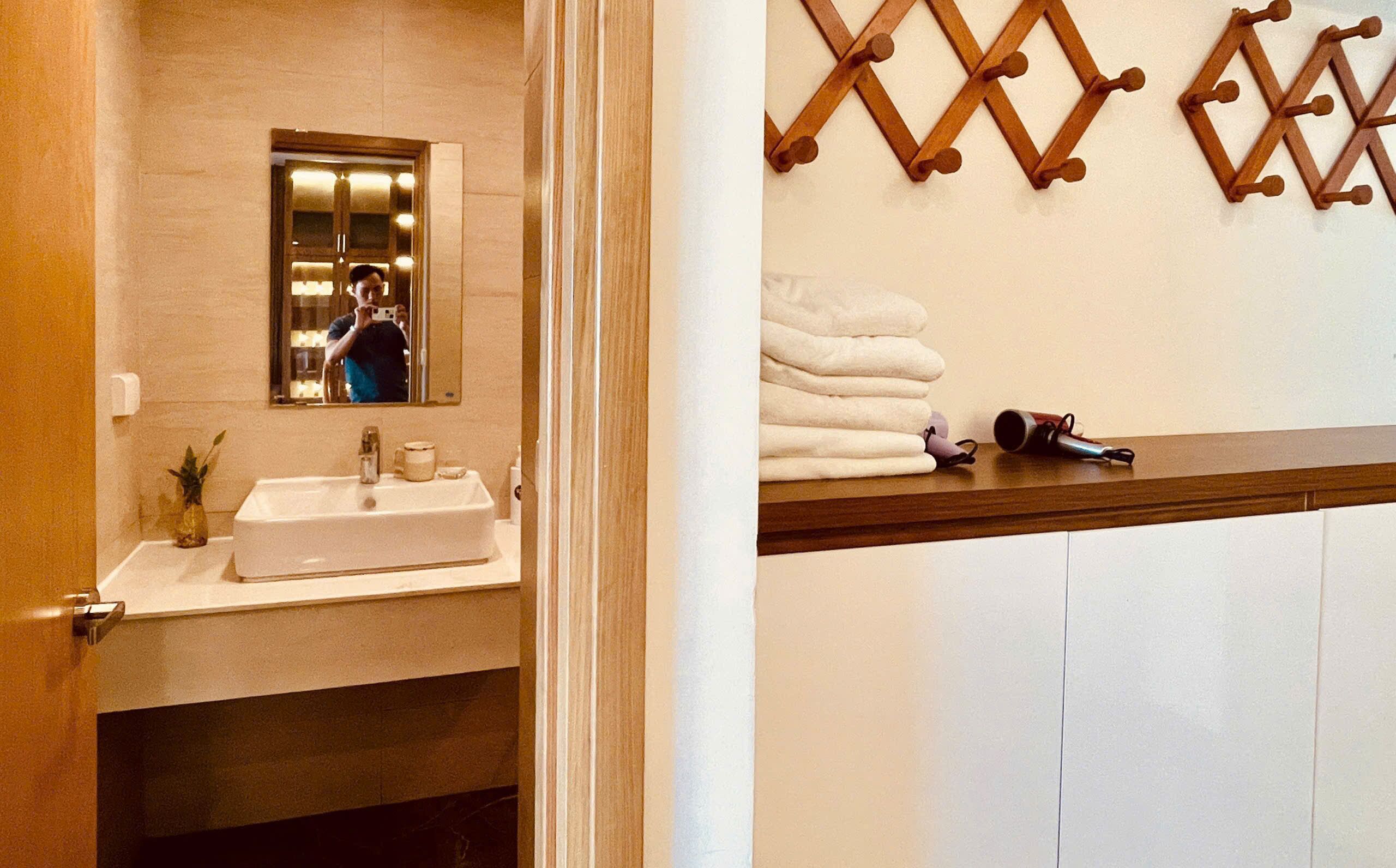 A bathroom with a sink, mirror, towel rack, and a towel dispenser.