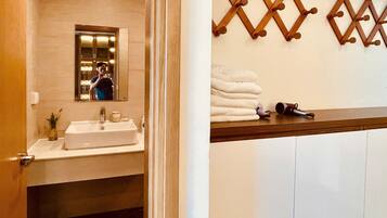 A bathroom with a sink, mirror, towel rack, and a towel dispenser.