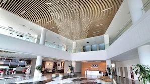 Een ruime lobby met een hoge plafond, meerdere zithoeken en een receptiebalie.