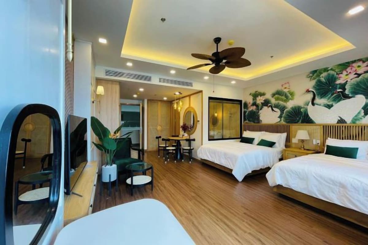 A hotel room with two beds, a ceiling fan, a dining area with a table and chairs, and a large mirror.