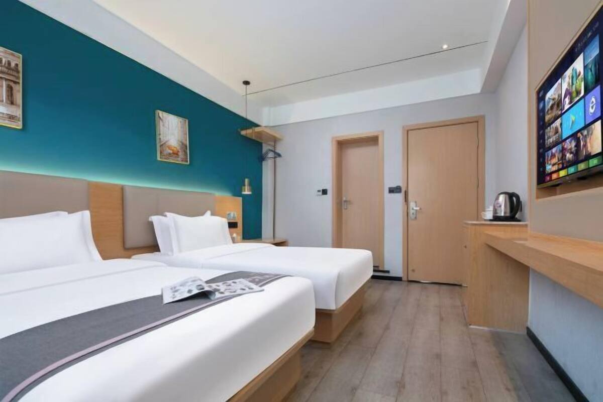 A hotel room with two beds, a desk, a TV, and a door.
