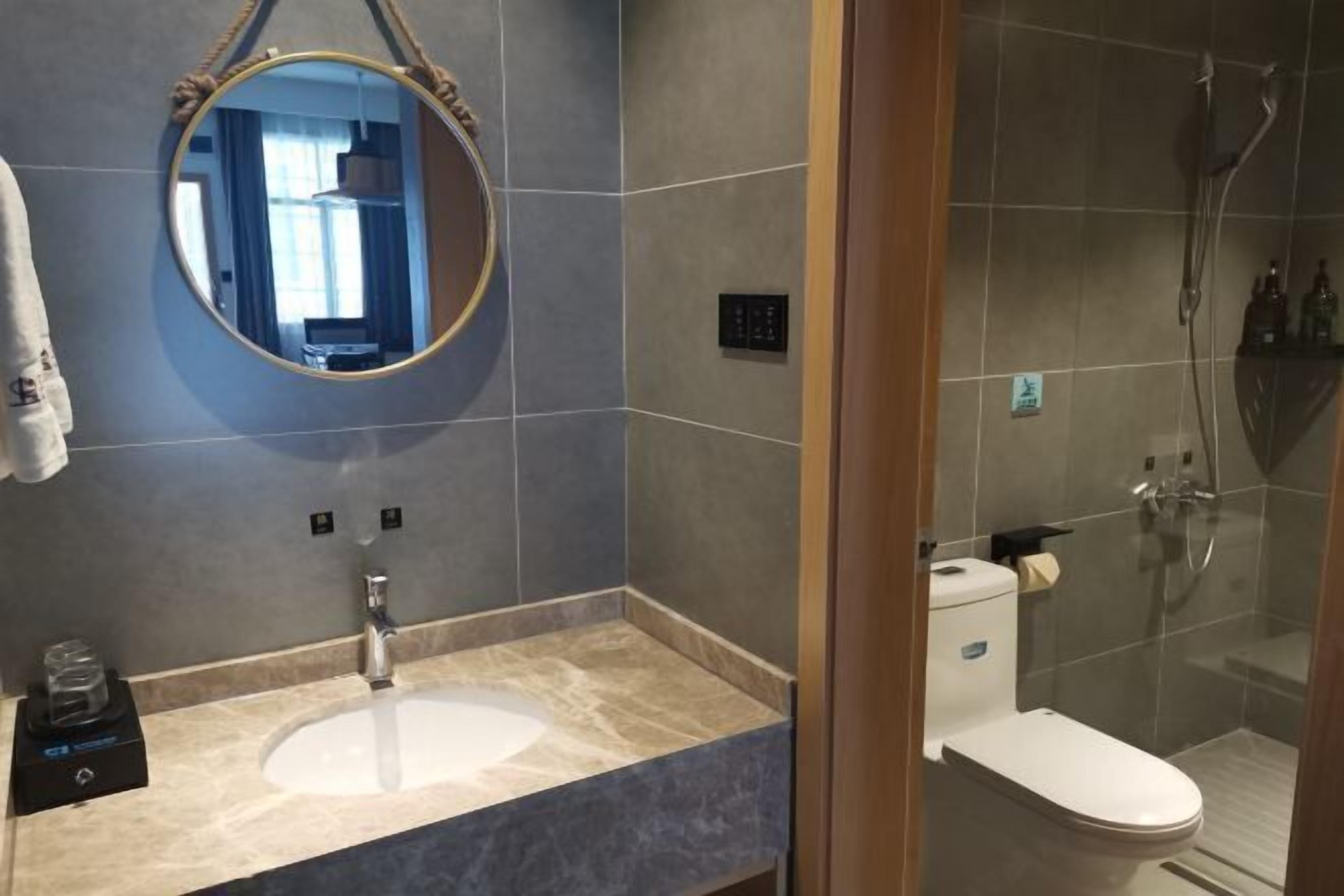 A bathroom with a round mirror, a sink, a toilet, and a shower.