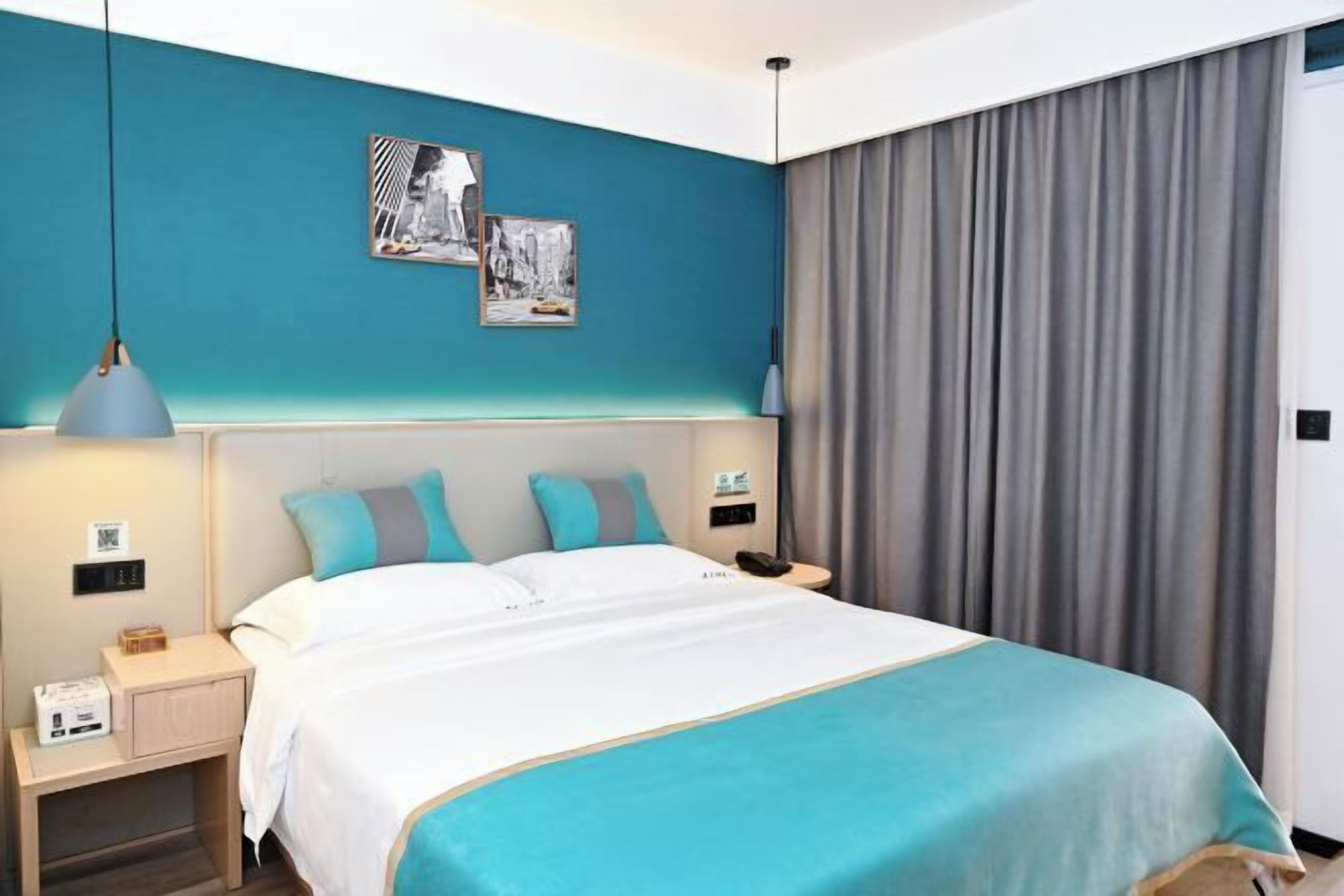 Habitación de hotel con cama, mesitas de noche, lámpara de pared y un amplio ventanal con cortinas.