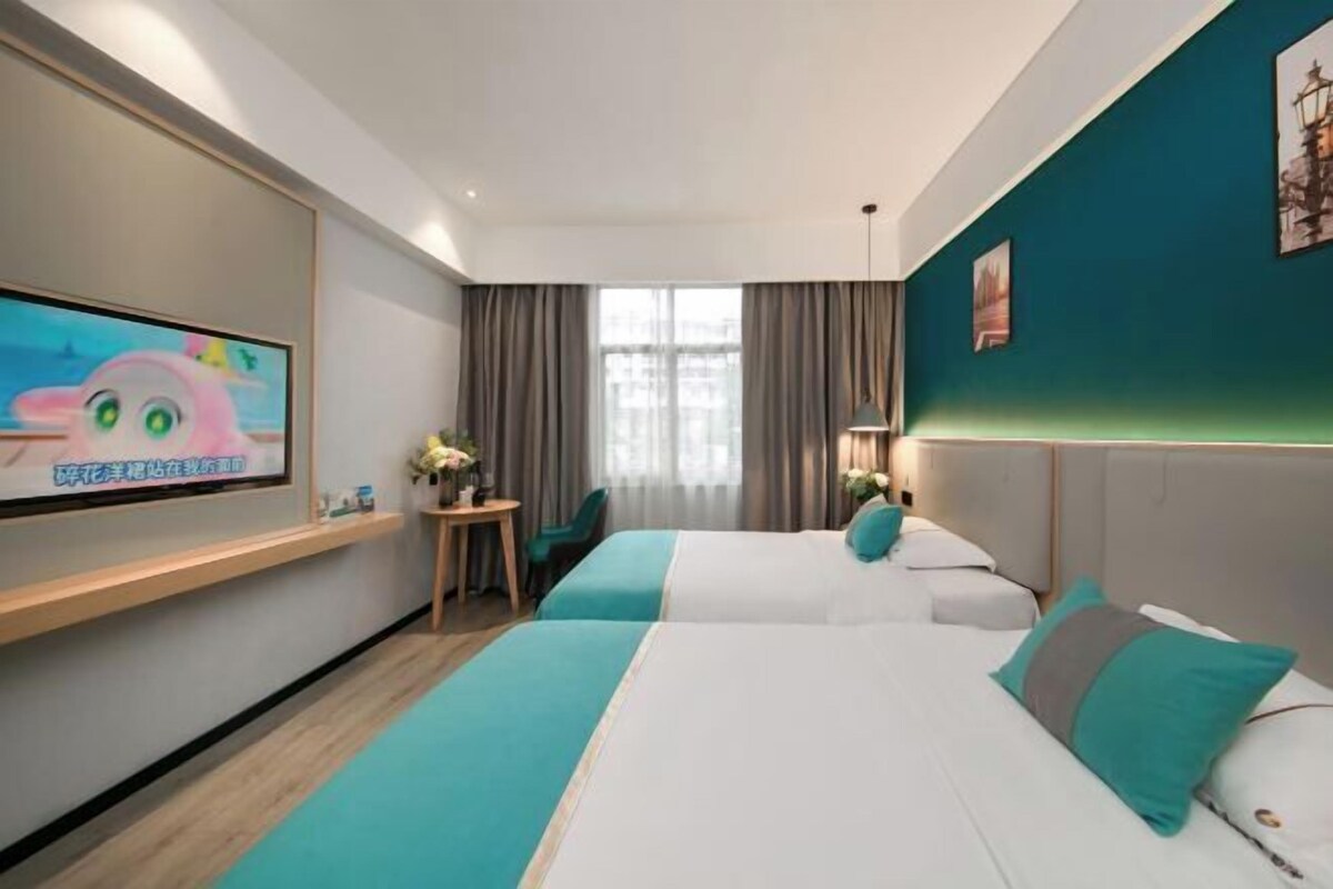 A hotel room with two beds, a TV on the wall, a desk, and a window with curtains.