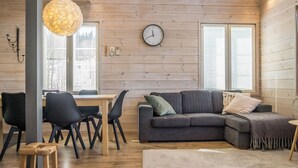 A cozy living room with a wooden floor, a gray sofa, a dining table with chairs, and a large window. - Pikku-pölly by Interhome (Sotkamo)