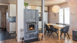 A modern kitchen with a stone fireplace, wooden flooring, and a dining area with a table and chairs. - Pikku-pölly by Interhome (Sotkamo)