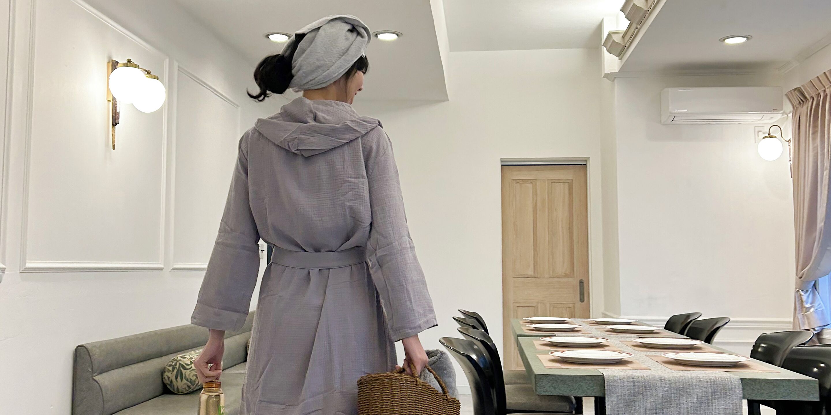 A person walking towards a dining area with a table set for a meal, a sofa, and a door in the background.