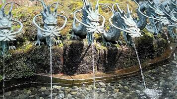 A row of dragon statues with water flowing from their mouths, set against a moss-covered rock surface.