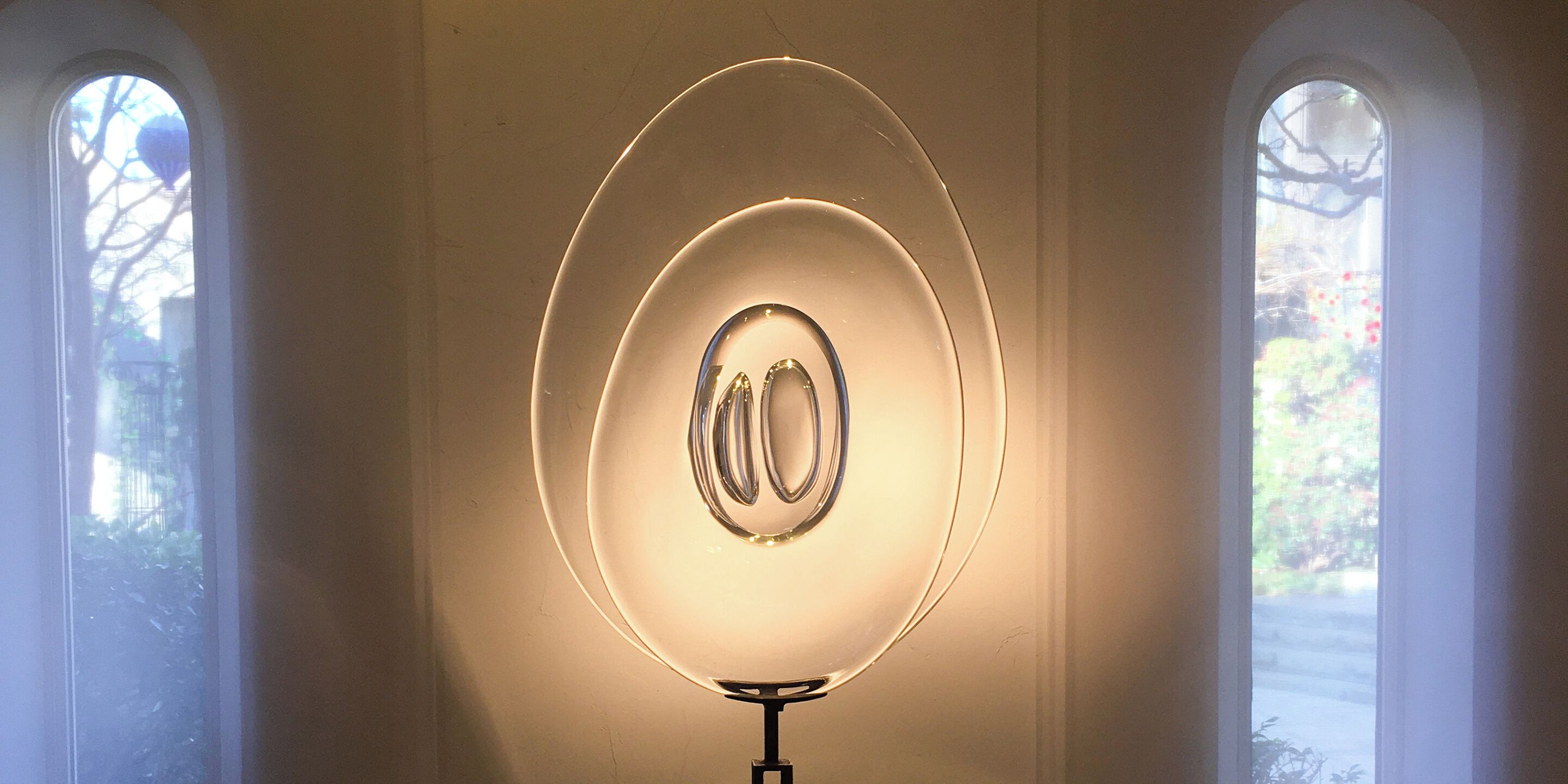 A room with a circular light fixture centered on the wall, flanked by two arched windows.