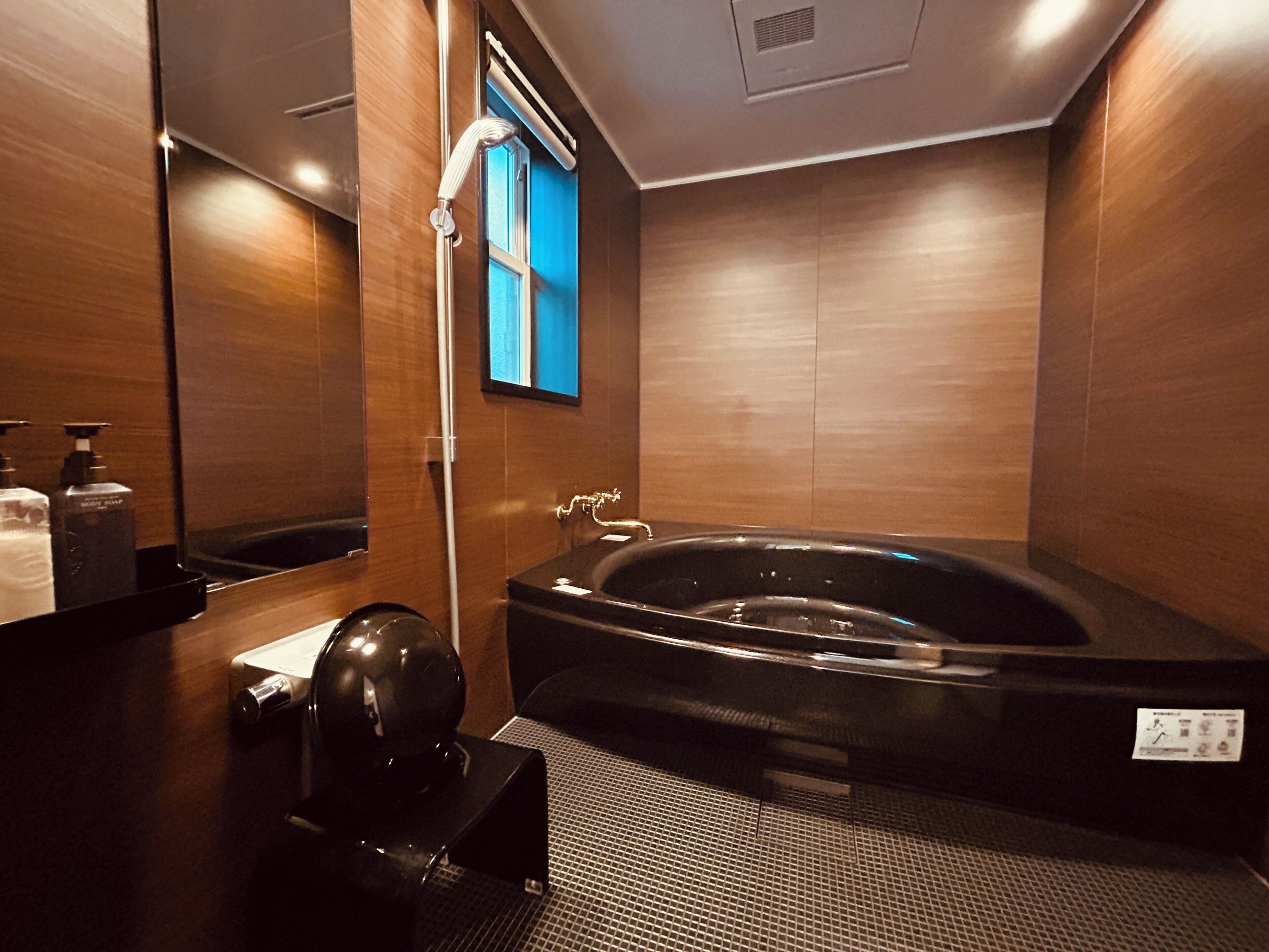 Un baño moderno con una bañera negra grande, un espejo y paredes de madera.