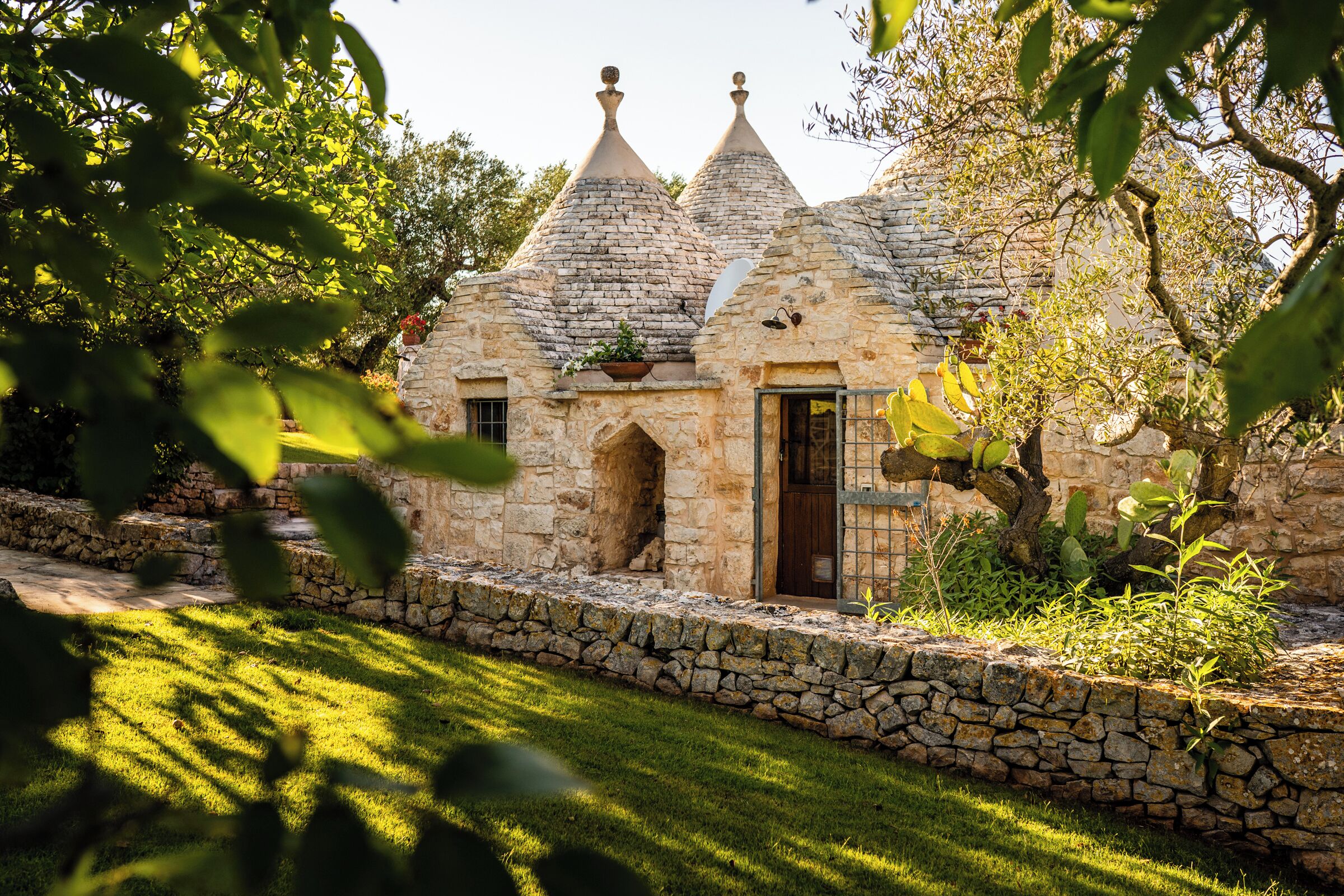 Un cottage in pietra con tetto di paglia, circondato da un muro in pietra e rigogliosa vegetazione.
