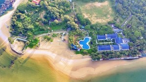 An aerial view of a coastal property with a swimming pool, beach access, and multiple buildings.