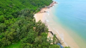 A coastal landscape with a beach, dense greenery, and a clear view of the ocean.