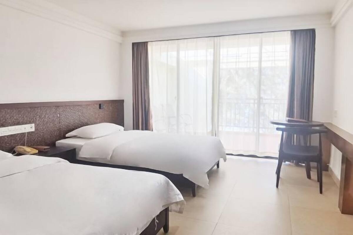 Hotellihuone, jossa on kaksi sänkyä, työpöytä ja suuri ikkuna, jossa on verhot.