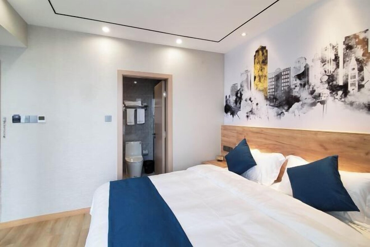 A hotel room with a bed, a cityscape mural, a wooden headboard, and a door leading to a bathroom.
