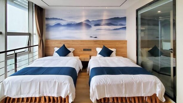 Habitación de hotel con dos camas, cabecero de madera, un ventanal grande y vistas a montañas.