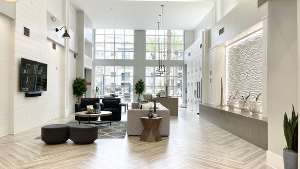 A spacious hotel lobby with a high ceiling, large windows, a modern fireplace, and a seating area with a coffee table and ottomans.