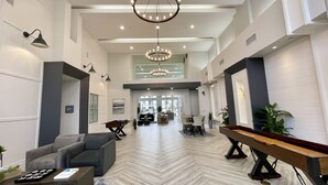 A spacious lobby with a high ceiling, modern chandeliers, and a pool table.