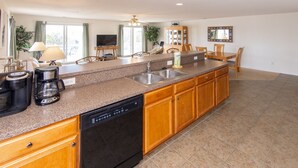 A modern kitchen with granite countertops, wooden cabinets, a dishwasher, and a dining area with a table and chairs.