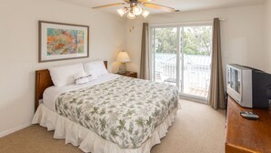 A bedroom with a bed, a ceiling fan, a TV, and a balcony with a railing.