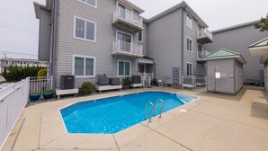 A residential building with a swimming pool, outdoor seating, and a fenced area.