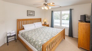 A bedroom with a wooden bed, a nightstand with a lamp, a small table with towels, a wooden cabinet, and a ceiling fan.