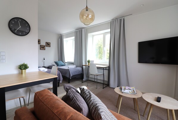 A modern hotel room with a bed, a sofa, a desk, a TV, and a large window.