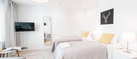 A modern hotel room with two beds, a flat-screen TV, a mirror, and a wall-mounted deer head artwork.